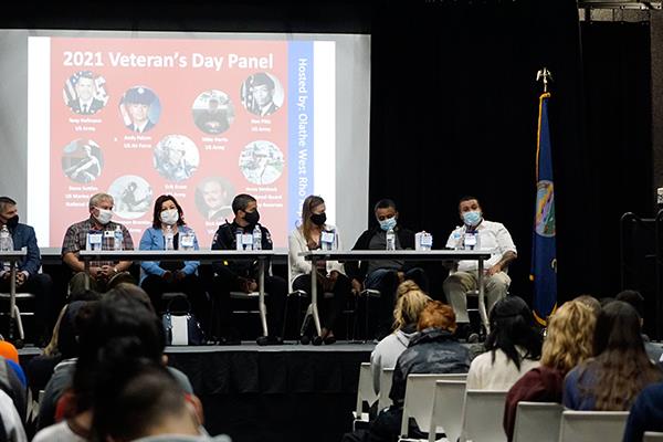 man seated on stage addresses students