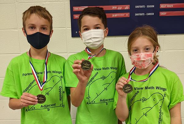 photo of three students wearing team shirts and medals