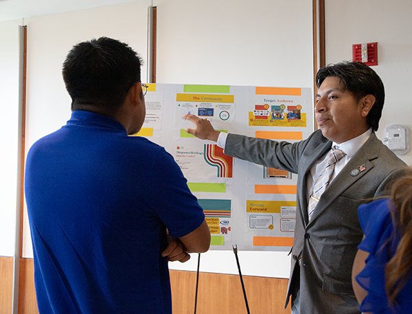 Brandon points to display board and explains his project