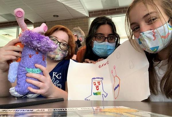 three girls gather close with their drawing and stuffed animal