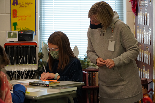 teacher looks over student's shoulder at classwork