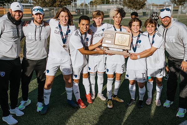 boys soccer team gathers with state championship trophy