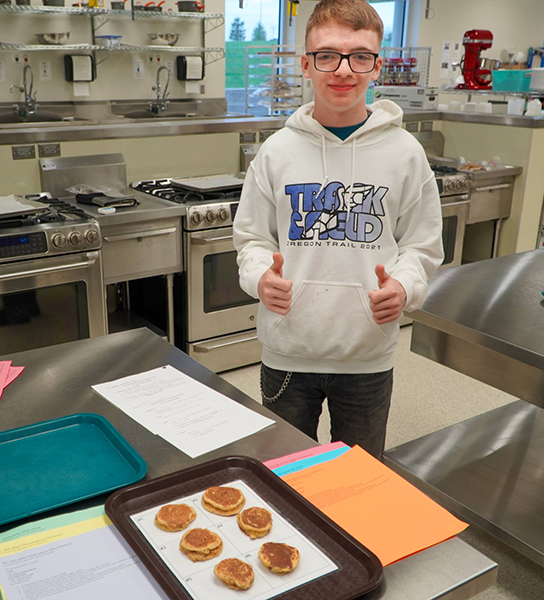 boy gives thumbs up sign beside plate of pancakes