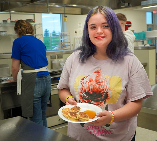 girl holds plate of pancakes toward camera