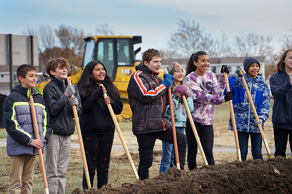 sixth graders stand holding shovels