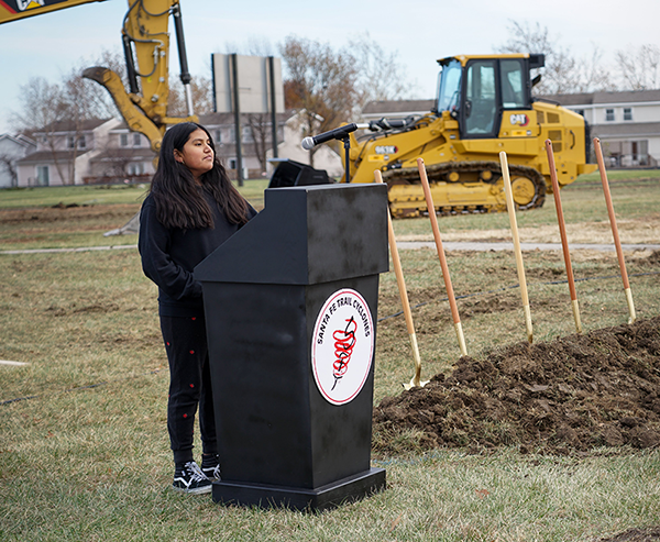 girl at podium, heavy equipment in background