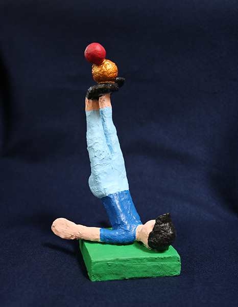 plaster sculpture of person lying on their back with legs up, balancing balls