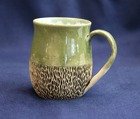 green stoneware mug with etchings around base