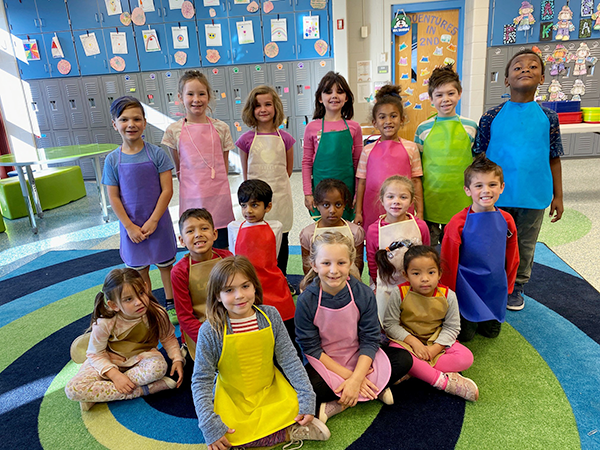 class of first graders pose for photo wearing aprons