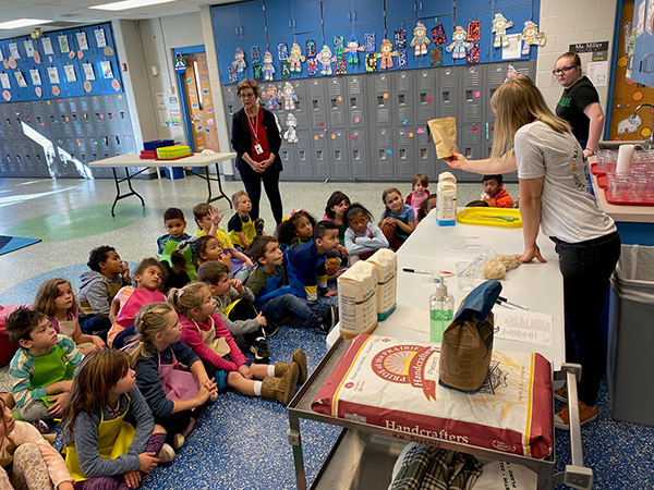 adult presenter shows bag of flour to students seated on floor