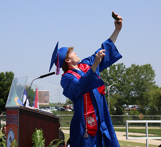 boy takes selfie while standing on stage at graduation