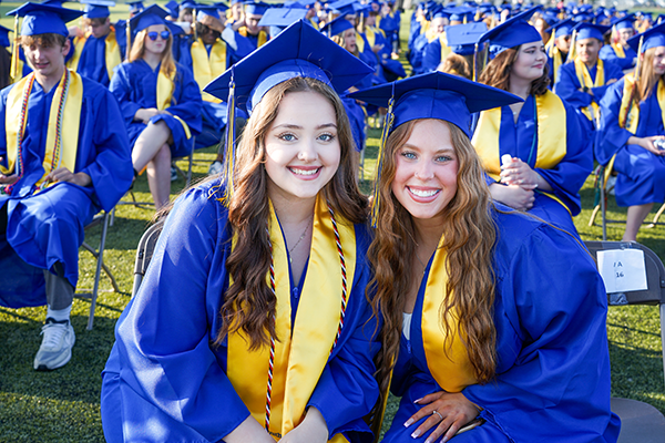 two girls wearing graduation attire smile for the camera