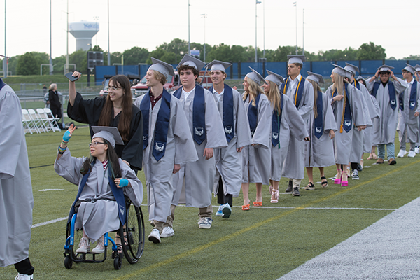 students wearing caps and gowns walk into graduation