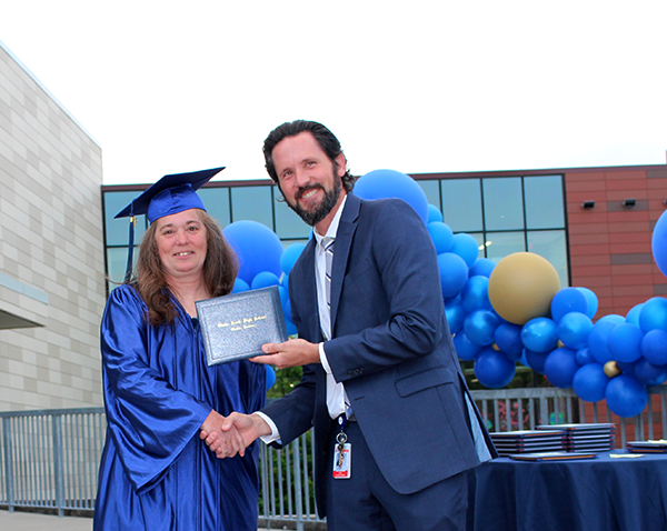 Man presents diploma to woman wearing graduation gown