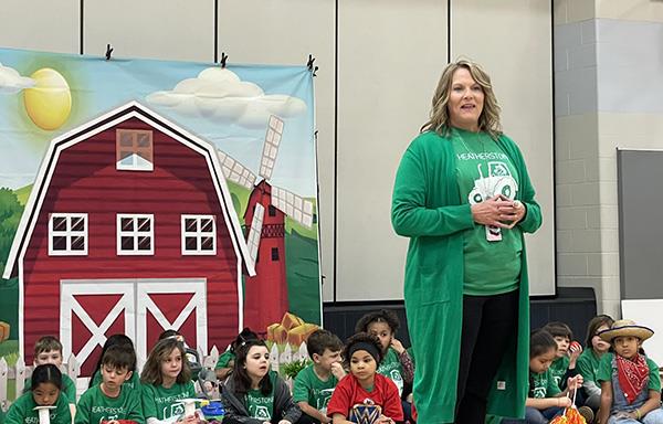 woman speaks to children wearing green shirts and farmer hats